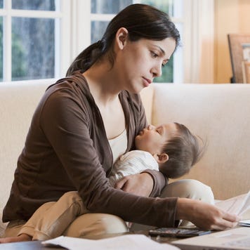 Hispanic woman paying bills online with sleeping baby