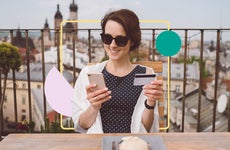 Woman sitting outside looking at phone and holding credit card