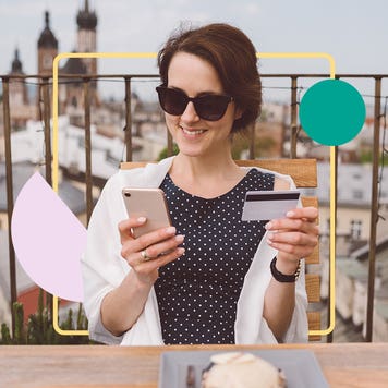 Woman sitting outside looking at phone and holding credit card