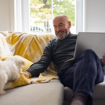 man using laptop, while petting Maltese dog