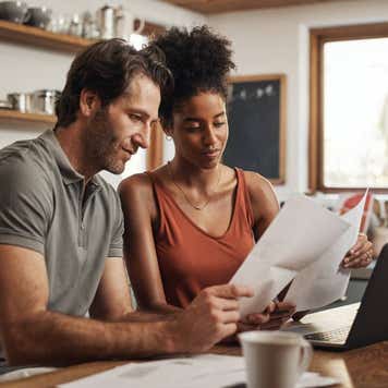 Cropped shot of a couple using their laptop and going through paperwork at home