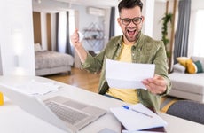 Man celebrating while going over paperwork and using a laptop at home