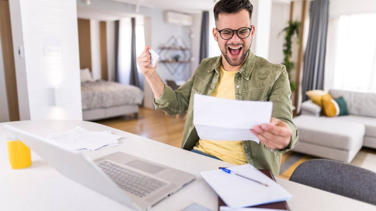 Man celebrating while going over paperwork and using a laptop at home