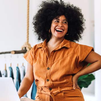 A Black female entrepreneur with natural hair smiles in front of a clothing rack.