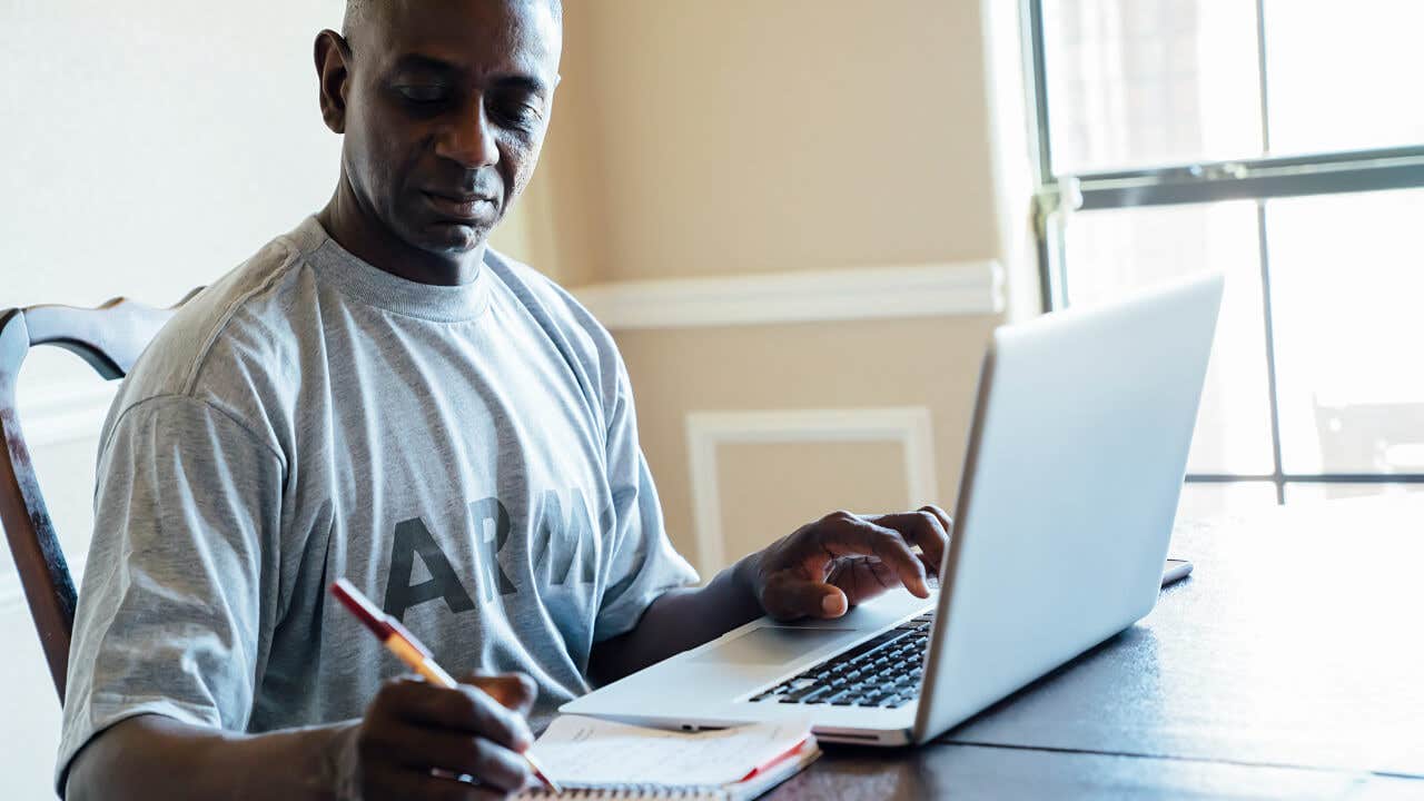 A black army veteran takes notes using a laptop.