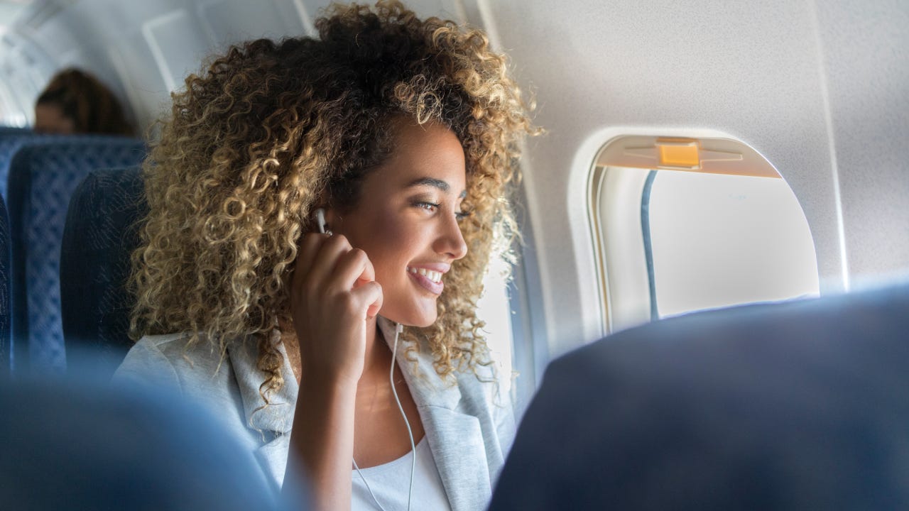 A young woman look out a plane window smiles