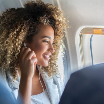 A young woman look out a plane window smiles