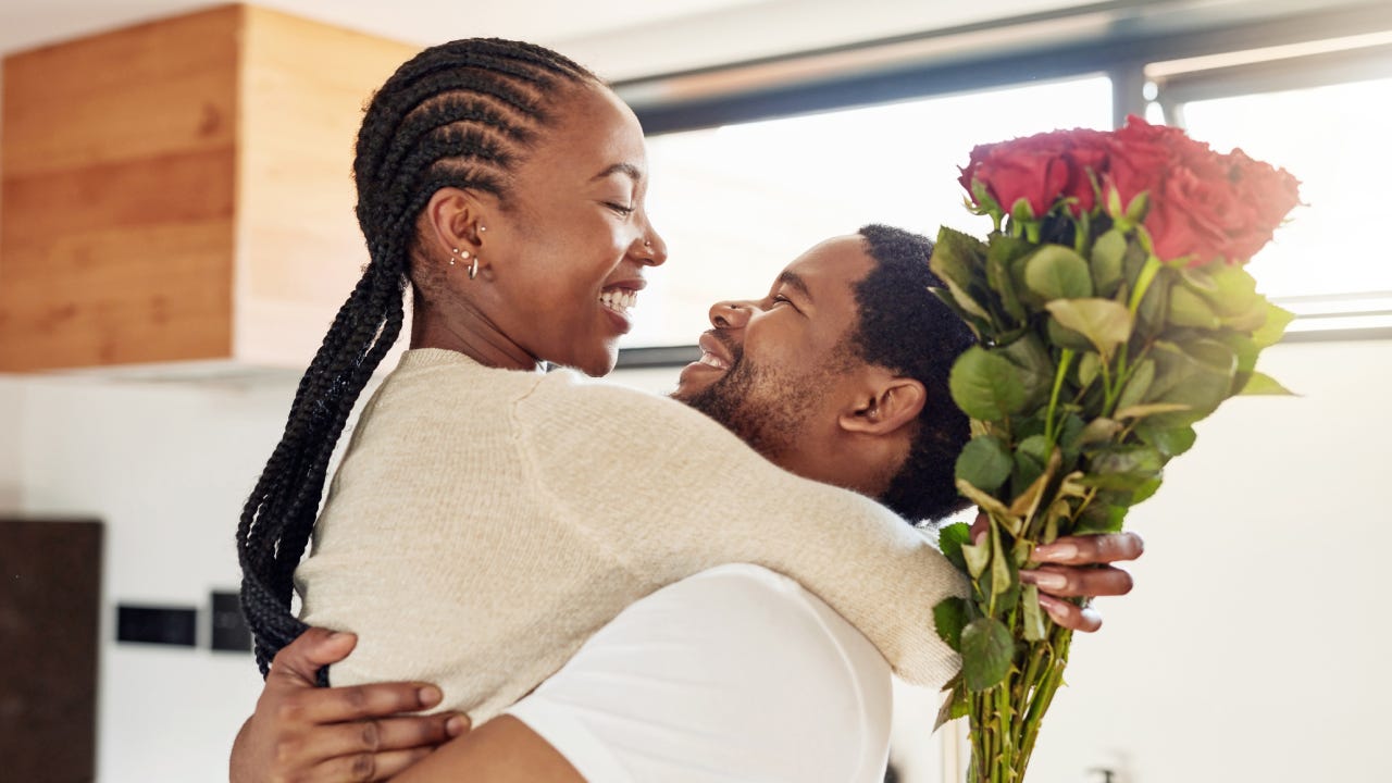 Shot of a young man surprising his wife with a bunch of flowers at home