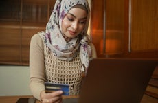 Asian Muslim woman holding a credit card and using the laptop for online shopping and online payment via the internet