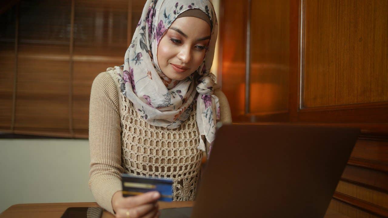 Asian Muslim woman holding a credit card and using the laptop for online shopping and online payment via the internet