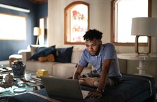 A young, Black man with a prosthetic leg using a laptop in a living room.
