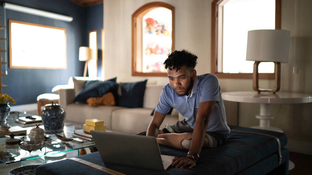 A young, Black man with a prosthetic leg using a laptop in a living room.
