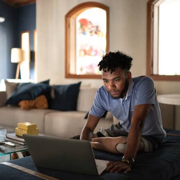 A young, Black man with a prosthetic leg using a laptop in a living room.