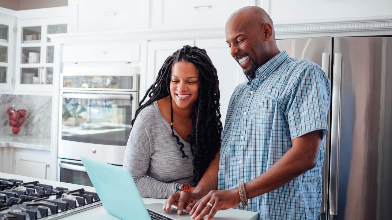 Man and woman using laptop in kitchen at home