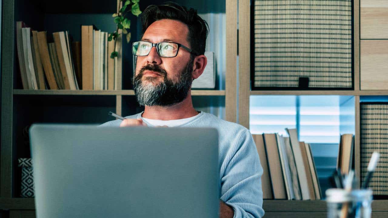 Thoughtful businessman with laptop sitting at desk in home office