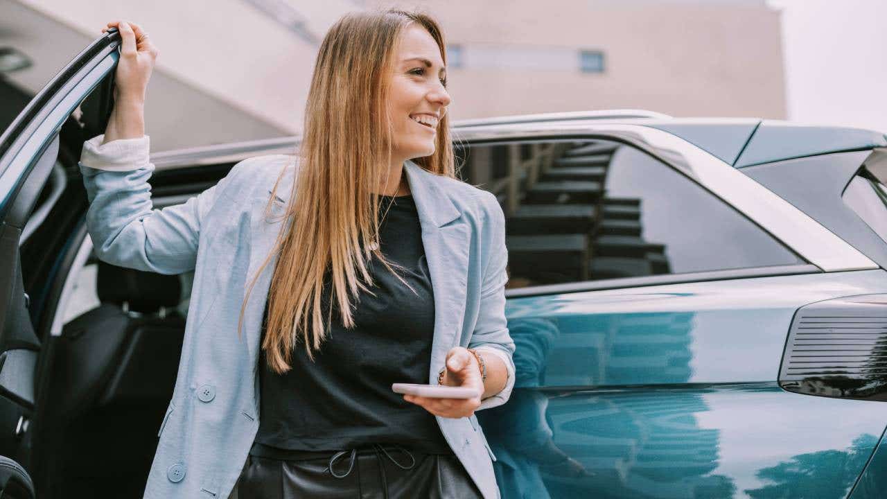 Happy woman with mobile phone standing by car door