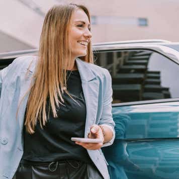 Happy woman with mobile phone standing by car door