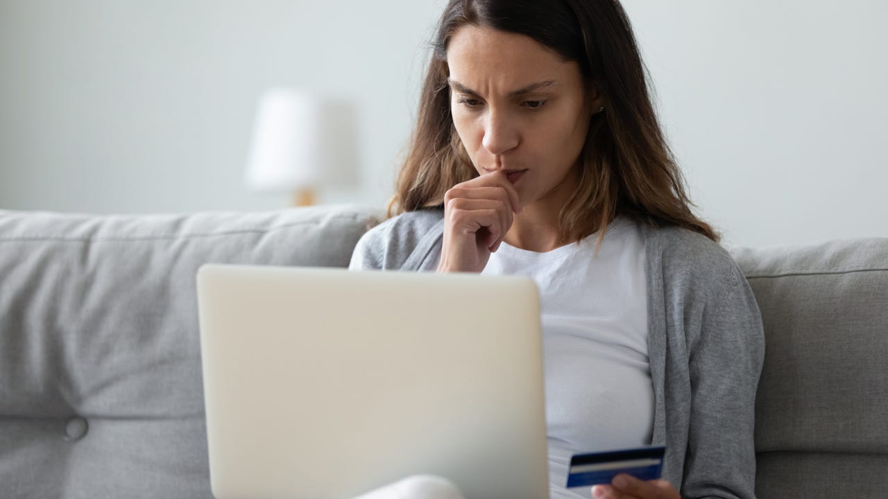 Concerned woman holding on lap computer in hand credit card