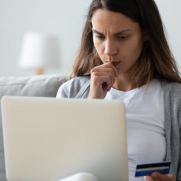 Concerned woman holding on lap computer in hand credit card
