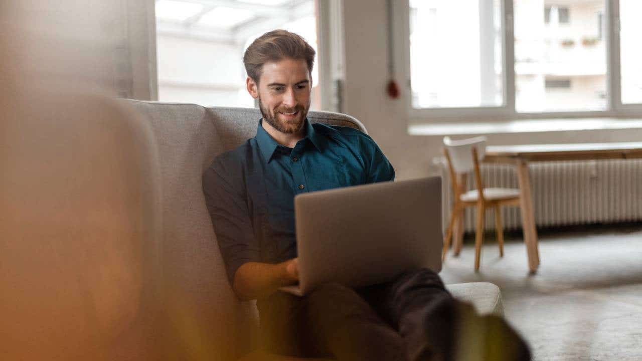 Portrait of young freelancer sitting on couch in a loft using laptop