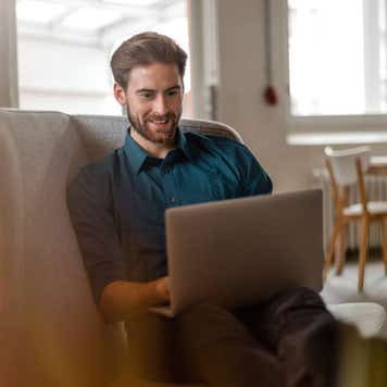 Portrait of young freelancer sitting on couch in a loft using laptop