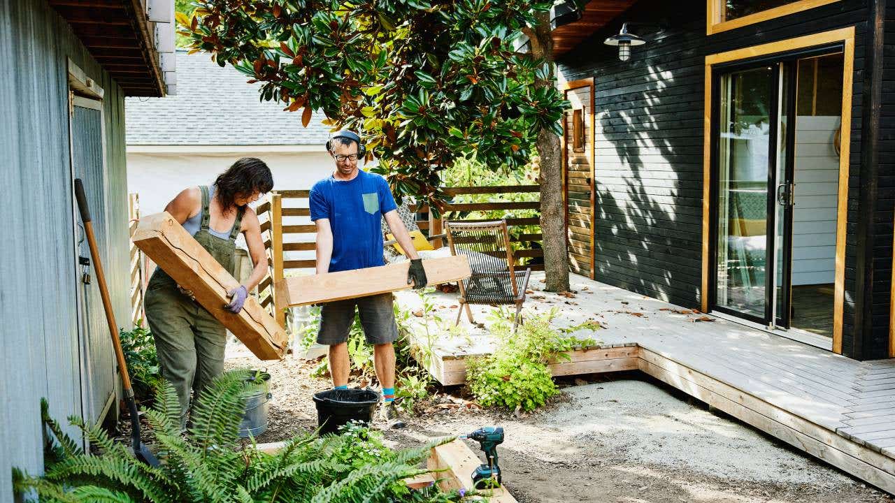 Couple carrying lumber to build raised garden beds in backyard