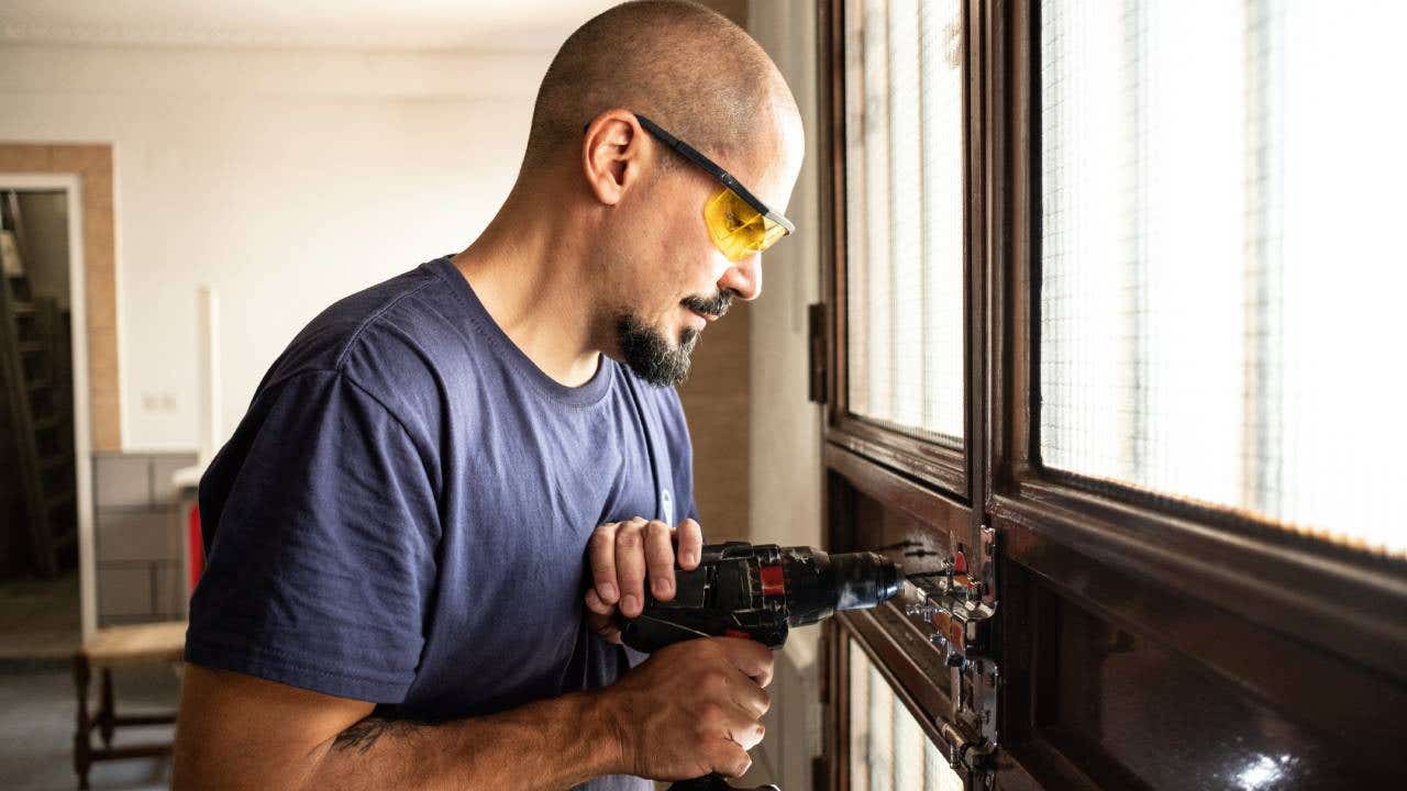 Locksmith changes a lock at home with a battery drill