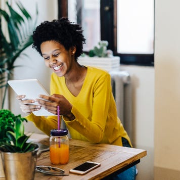 Young Black woman smiling at tablet sitting at a table