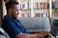 Man sitting on couch smiling at laptop while using it