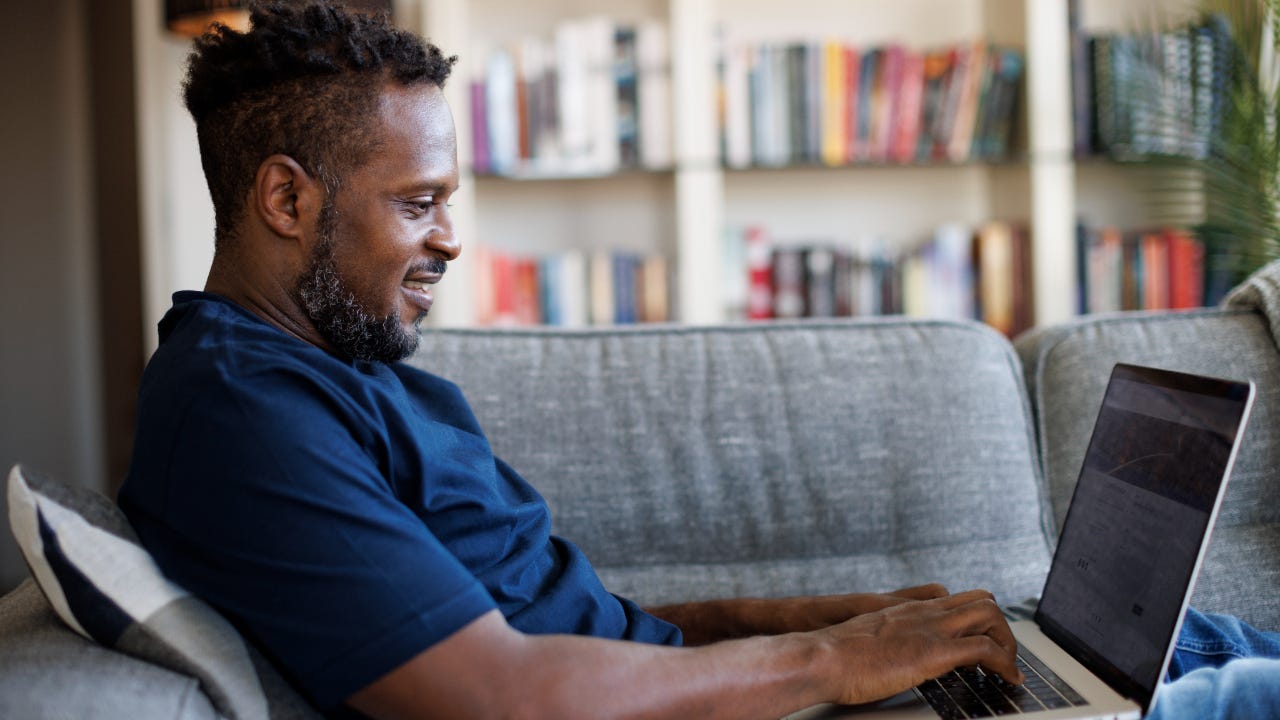 Man sitting on couch smiling at laptop while using it