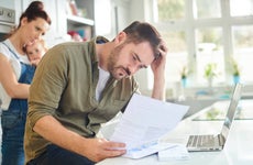 Man reviewing finances over kitchen counter with wife and child in the background.