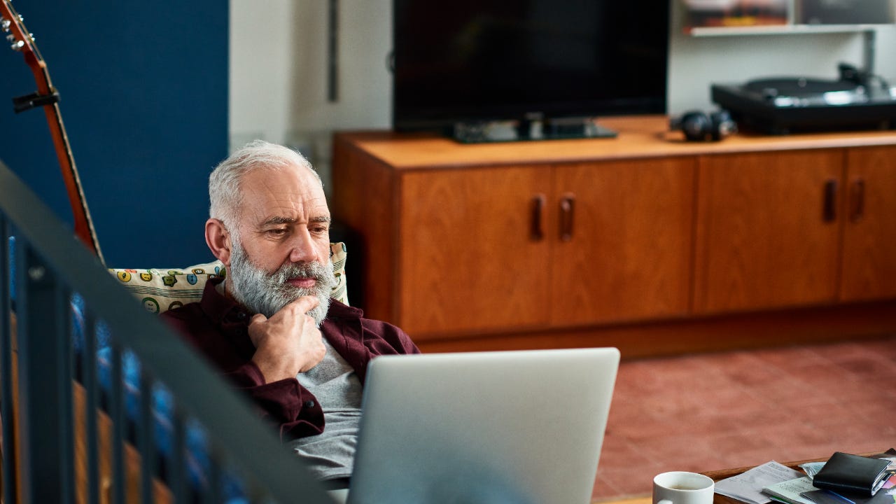 Older man on couch with laptop on lap looking thoughtful