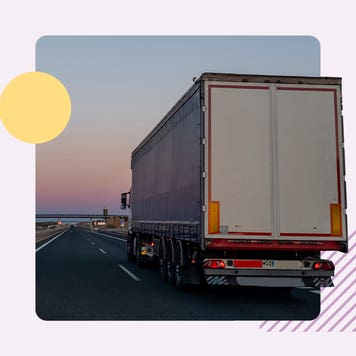 The back of a semi truck driving on a highway during sunset.