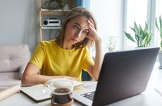 A white woman rests her head in her hand while staring at a laptop. She looks frustrated.