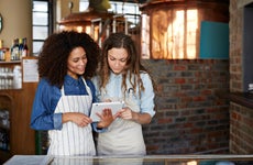 Two female restaurant owners, wearing aprons, look at a tablet