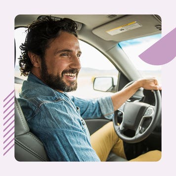 A smiling white man sits in the driver's seat of a car.