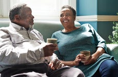 Smiling senior couple holding drinks talking while sitting on sofa at home