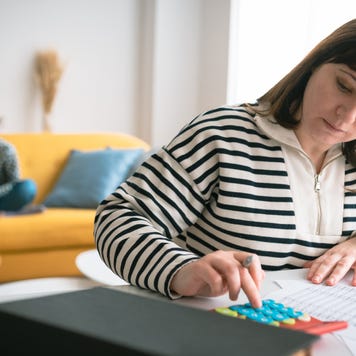 Woman managing the monthly family budget while her daughter plays with a dog in the background