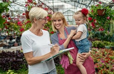 A small business owner smiles and goes over invoices in a greenhouse with her daughter and granddaughter standing nearby.
