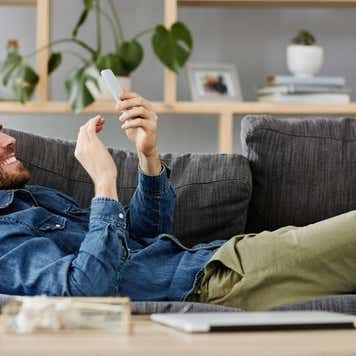 Shot of a young man using his mobile phone while laying on his couch at home