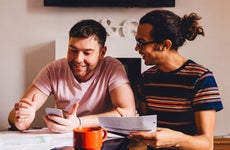Male couple looking through financial documents together in their home.