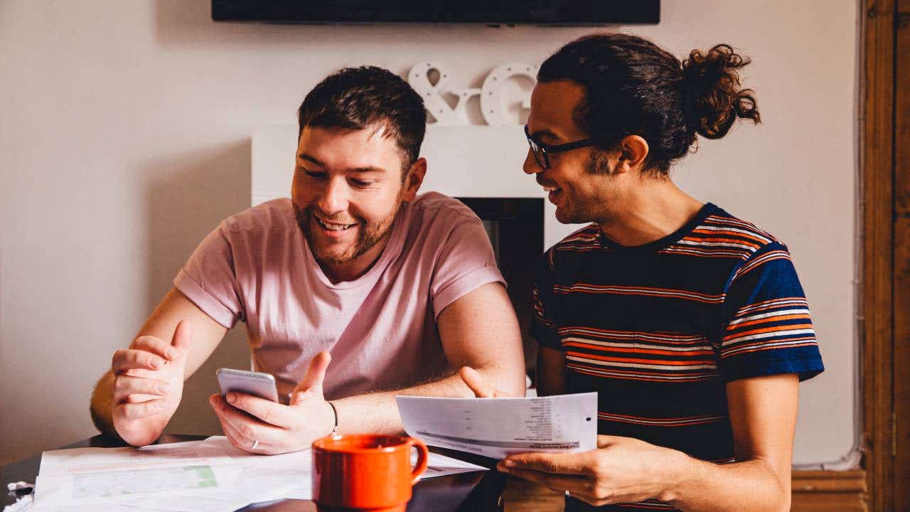 Male couple looking through financial documents together in their home.