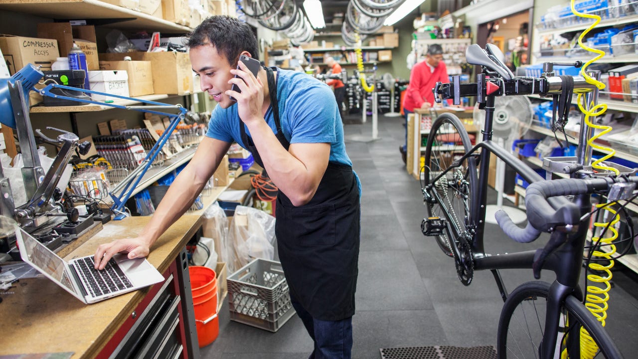 A business owner uses a cellphone and laptop in a bike repair shop