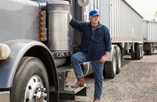 A semi-truck driver stands next to his truck.