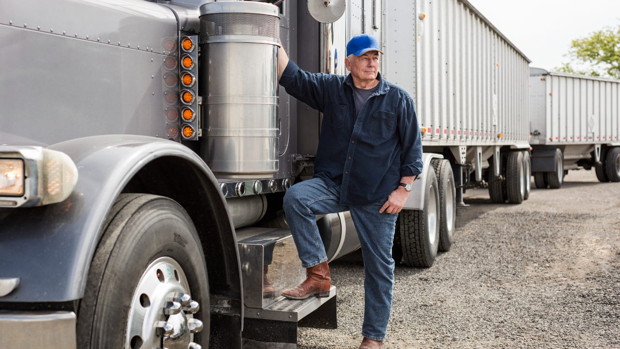 A semi-truck driver stands next to his truck.