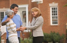 Couple shaking hands with real estate agent in front of house