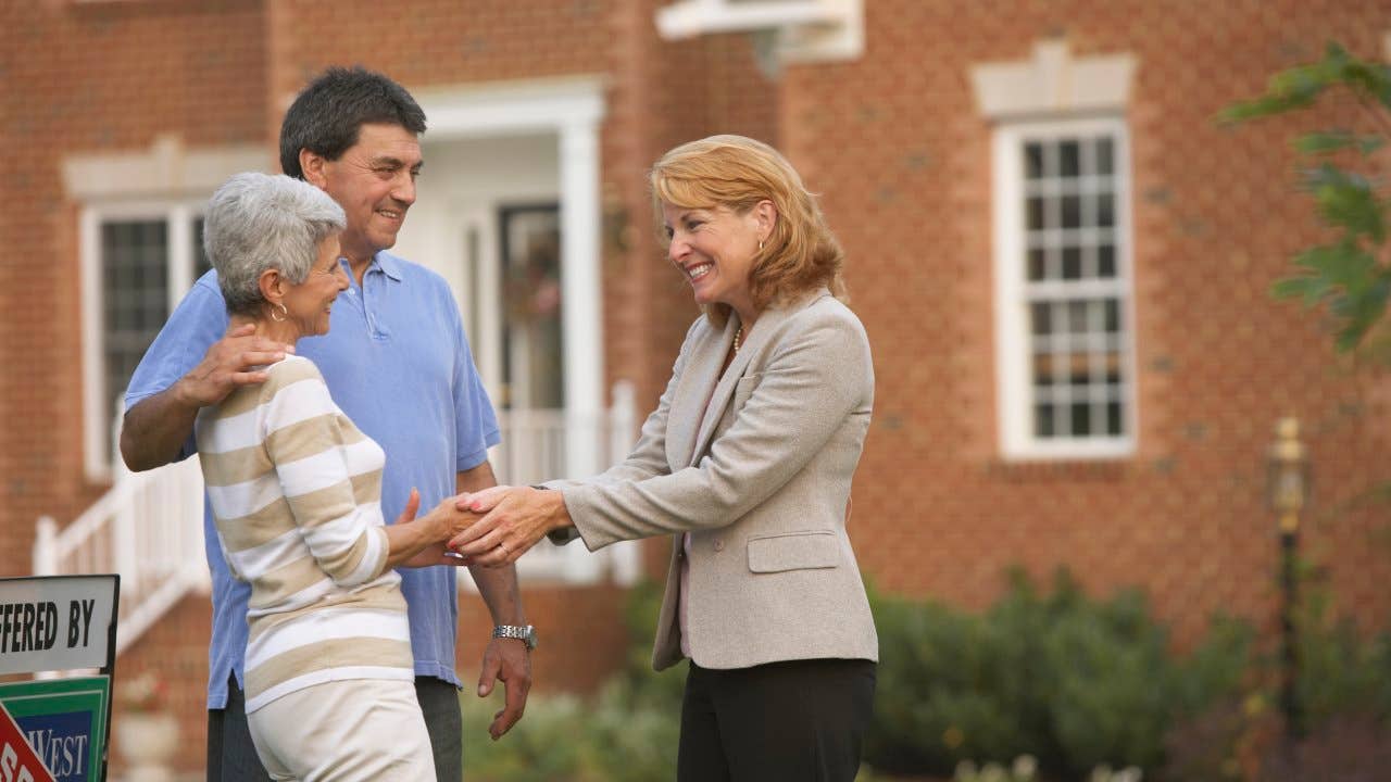 Couple shaking hands with real estate agent in front of house