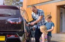 A father plugs in his electric vehicle at home while his two small children watch.