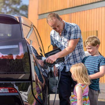 A father plugs in his electric vehicle at home while his two small children watch.