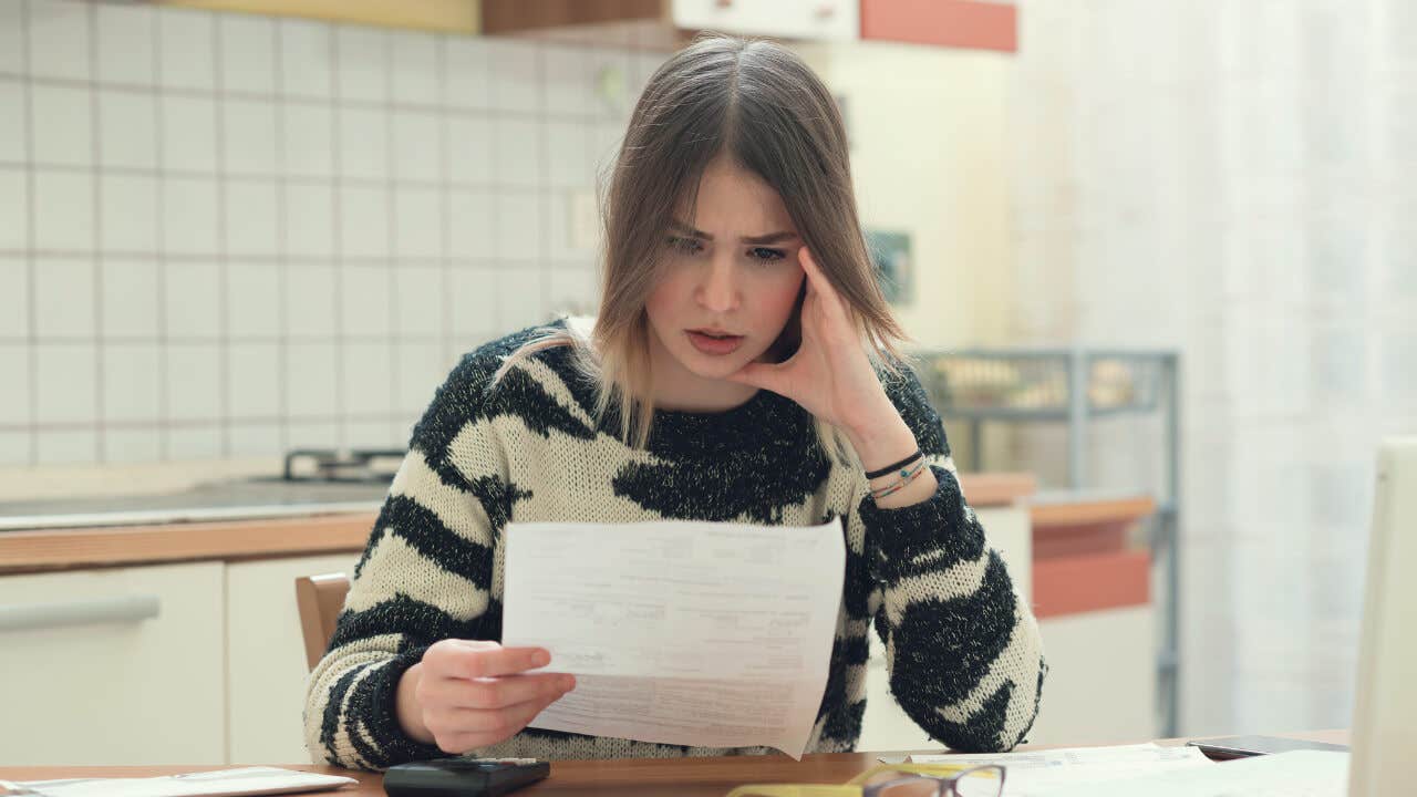 A young woman frowns worriedly at a document she is holding.